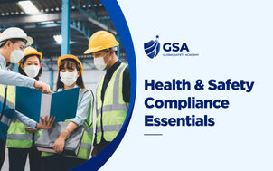 Global Safety Academy Health & Safety Compliance Essentials training banner showing a group of factory workers wearing hard hats, face masks, and high-visibility vests examining document binders